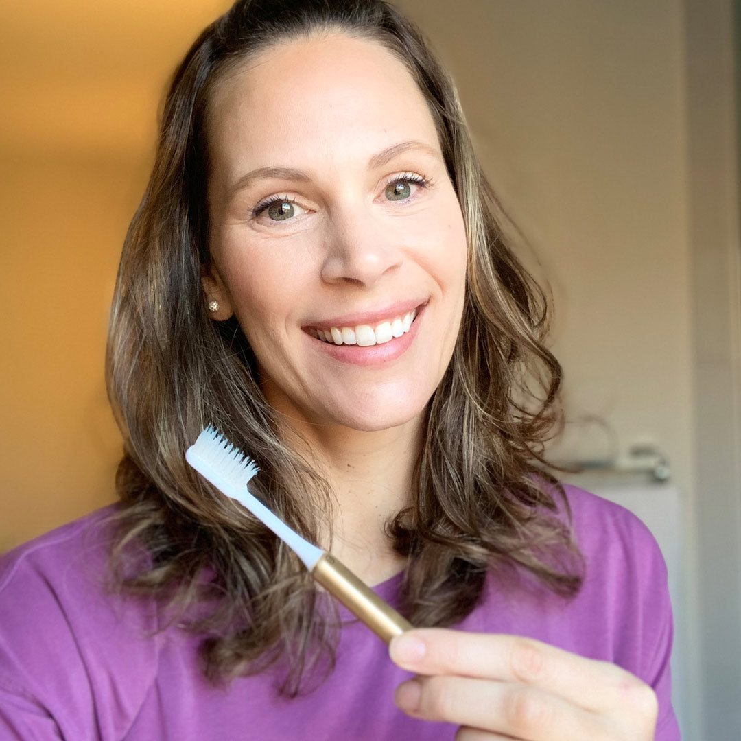 Woman smiling and holding a Gold sustainable Nada toothbrush with an aluminum handle and replacement brush head