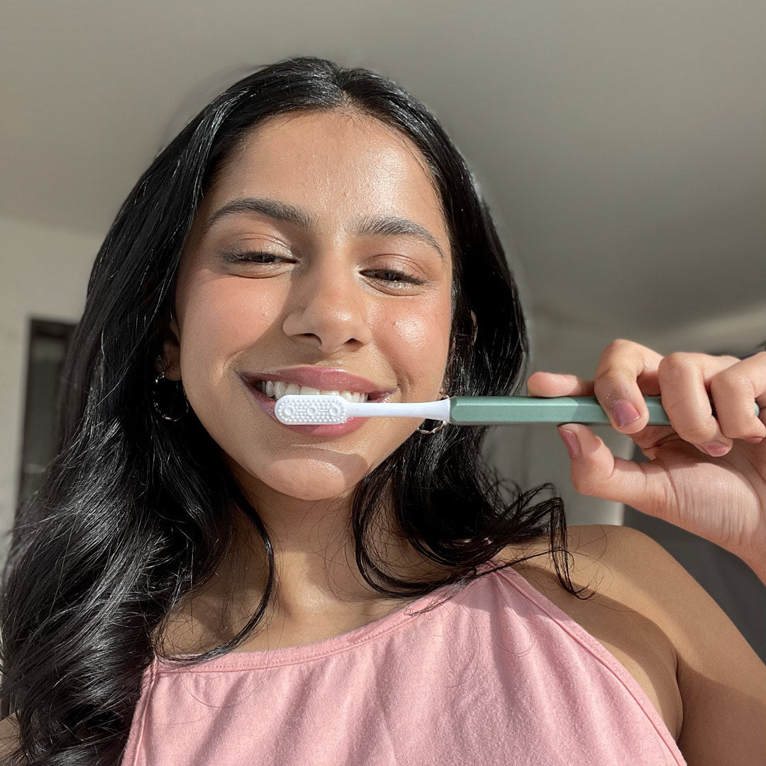 Young woman smiling and holding a Green sustainable Nada toothbrush with an aluminum handle and replacement brush head