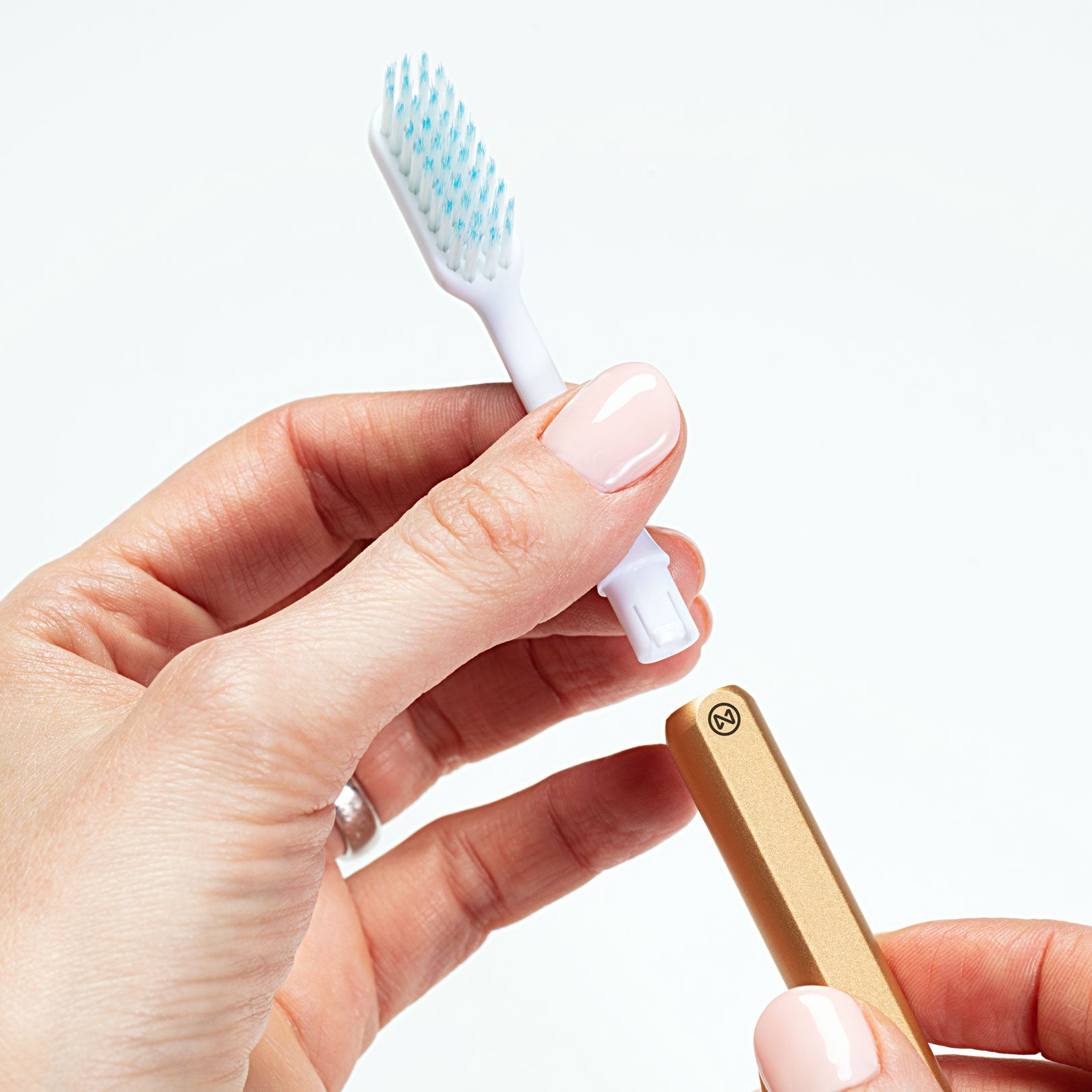 Gold Nada sustainable toothbrush handle in a hand with the brush head being removed
