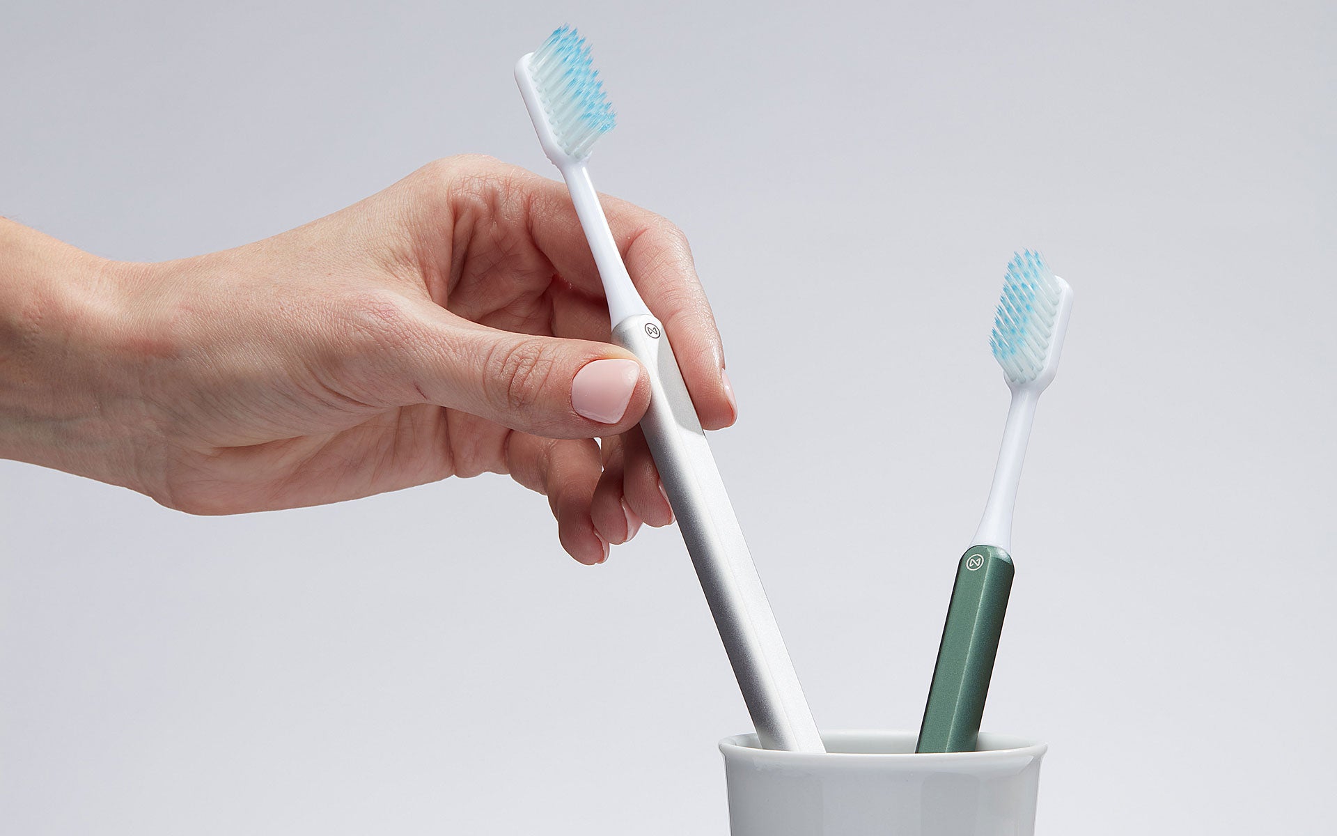 Hand removing for a Silver Nada toothbrush from a cup with a Green Nada toothbrush