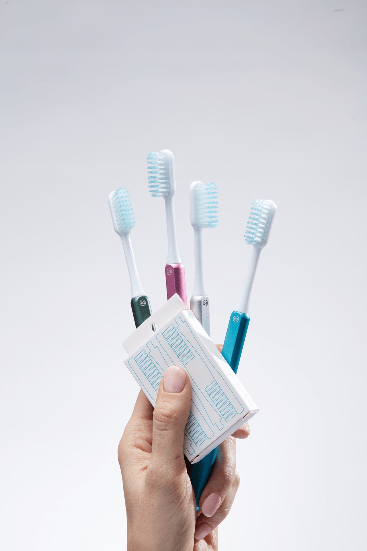 Hand holding four Nada toothbrushes fanned out with a box of replacement brush heads