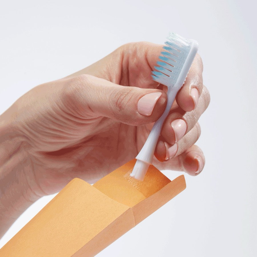 A hand placing a used Nada brush head into the pre-addressed return envelope