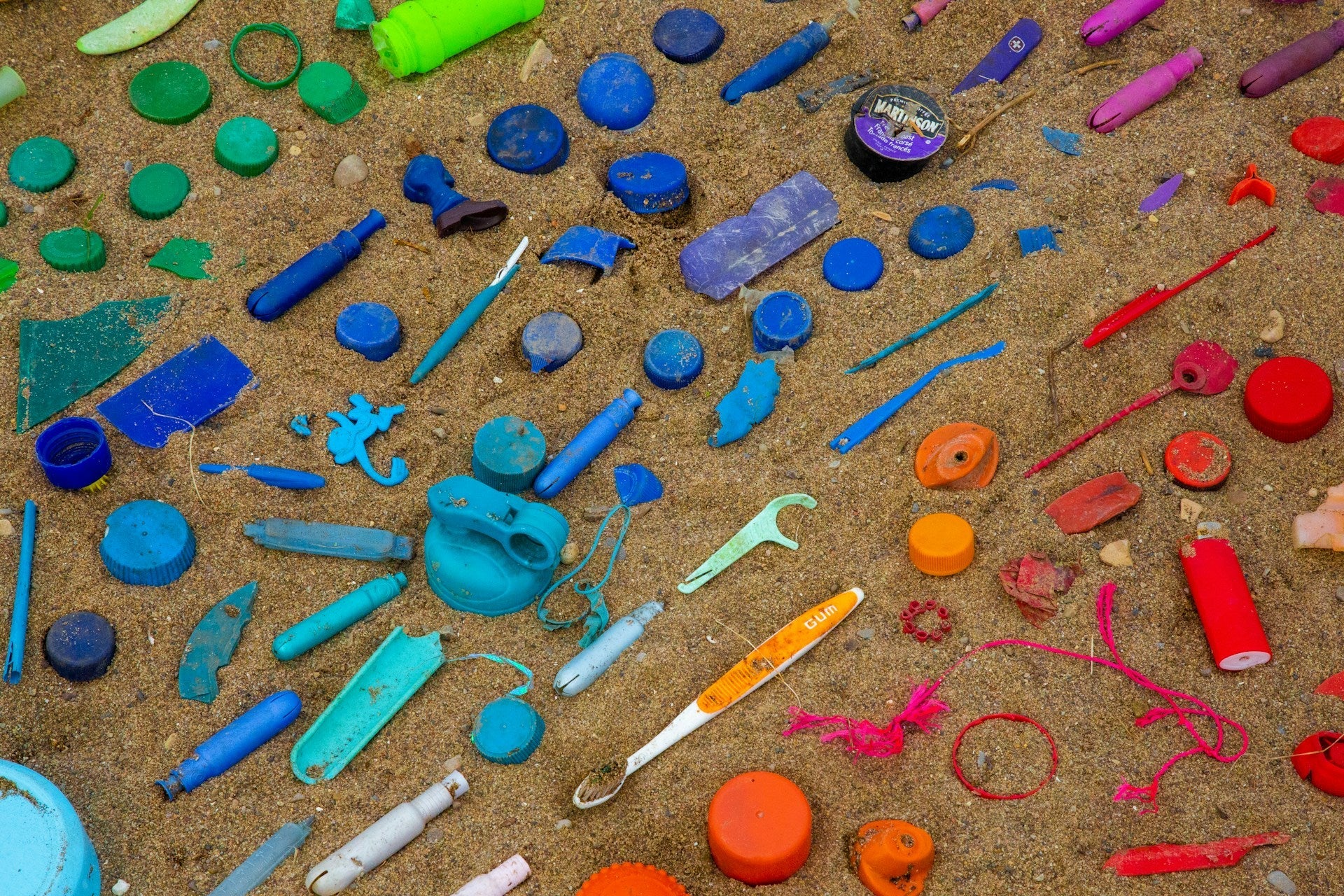 Colourful plastic items on a beach, including a disposable toothbrush and floss pick