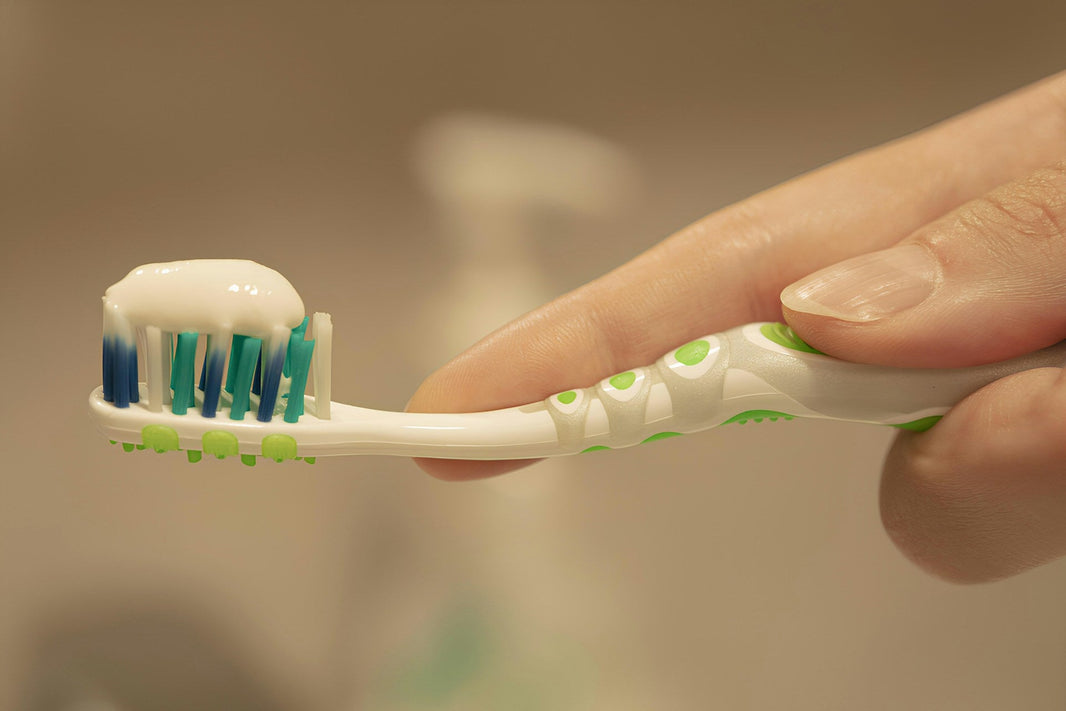 A hand holding a disposable toothbrush with some toothpaste on it