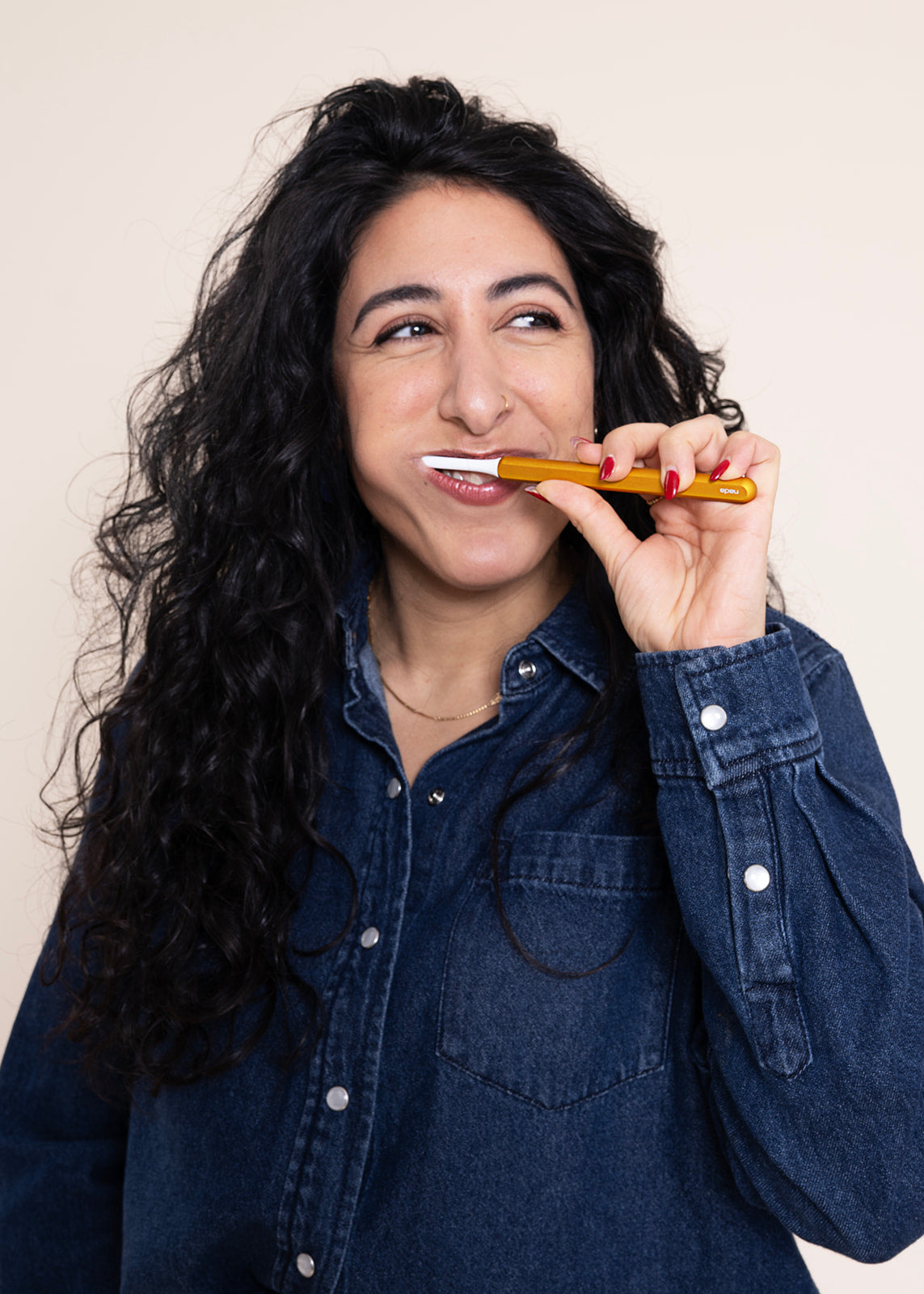 Woman brushing her teeth with a gold, eco-friendly Nada toothbrush. 