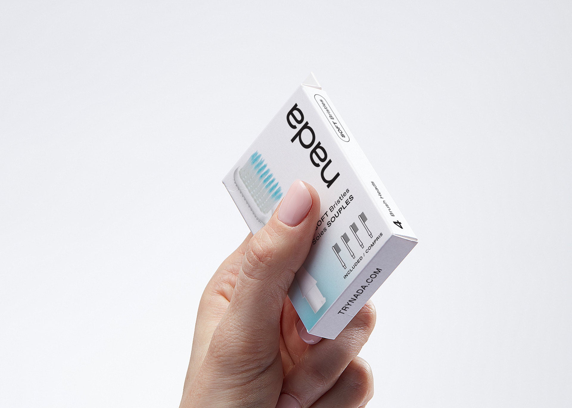 Hand holding a 4-pack of Nada recyclable toothbrush heads with Soft, floss-tip bristles