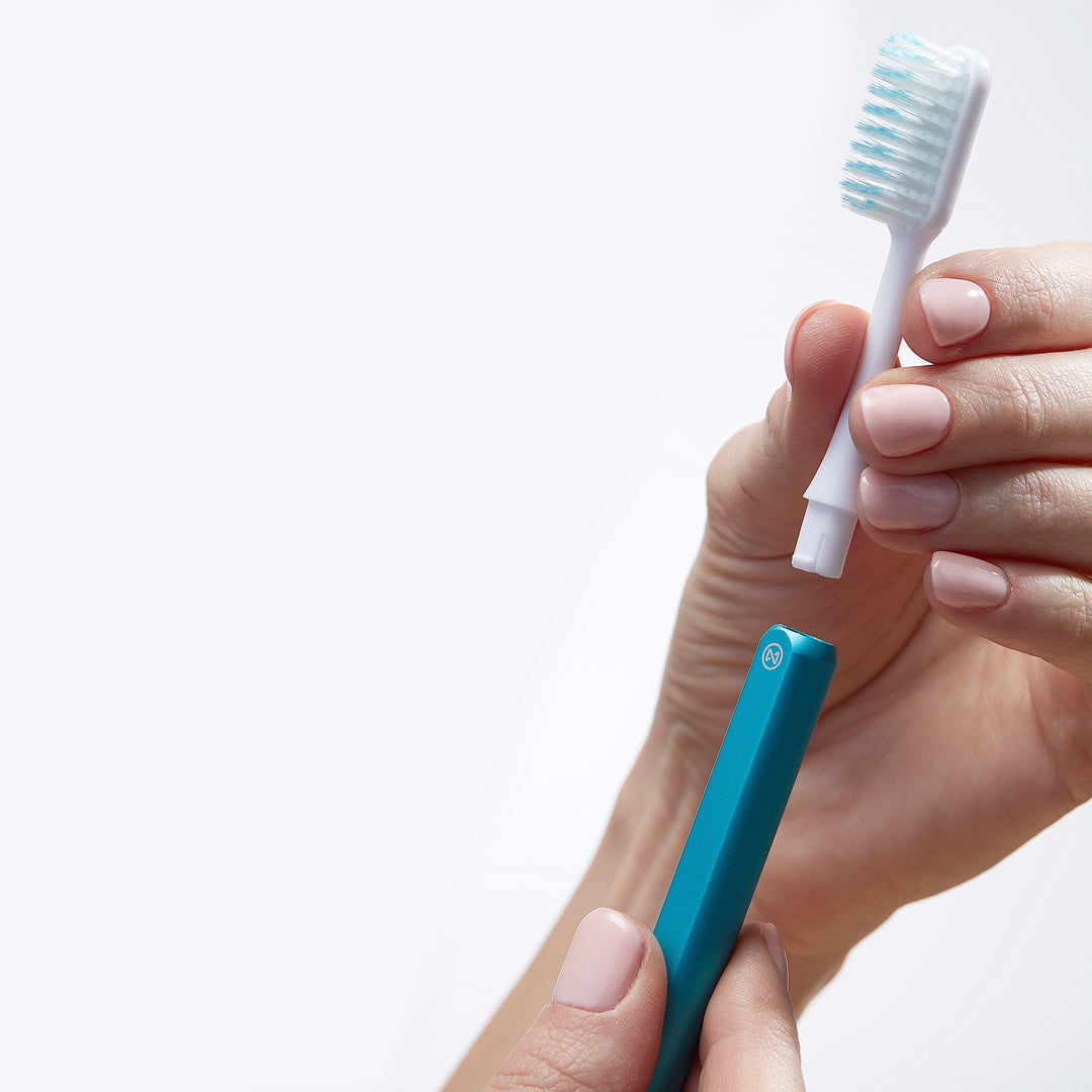 Hand removing a Nada toothbrush head from an Ocean Blue aluminum handle