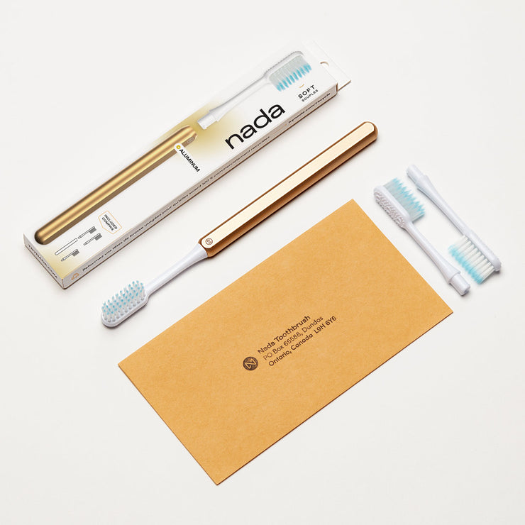 Gold Nada Eco-friendly Toothbrush with a metal handle, replacement brush heads and a return envelope