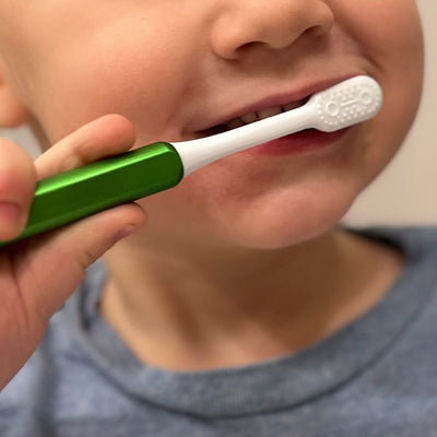 Child brushing with a lime green kids Nada eco-friendly toothbrush with a metal handle and replacement toothbrush heads