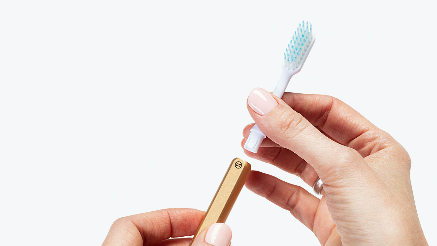 Gold Nada toothbrush handle with a brush head being inserted