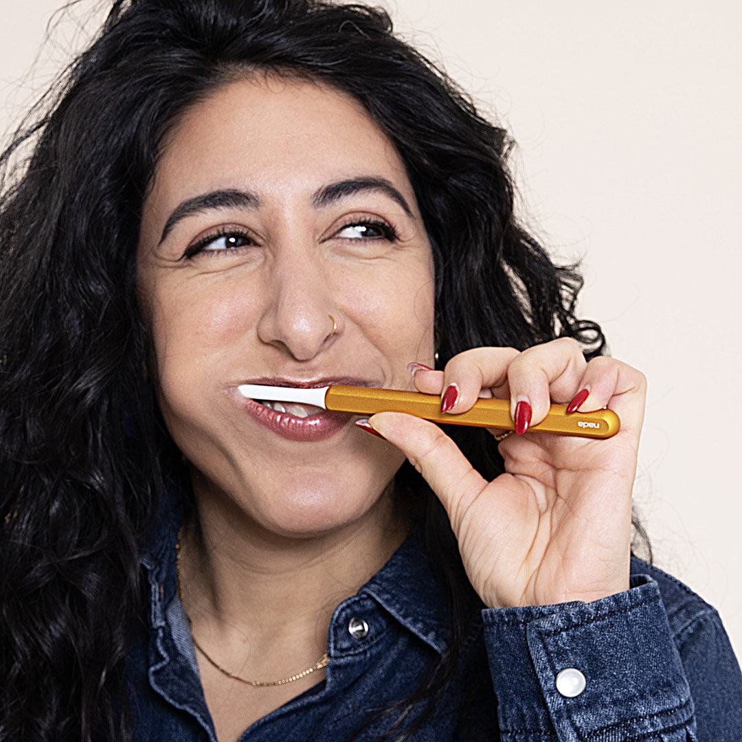Woman brushing with a sustainable Gold Nada Toothbrush